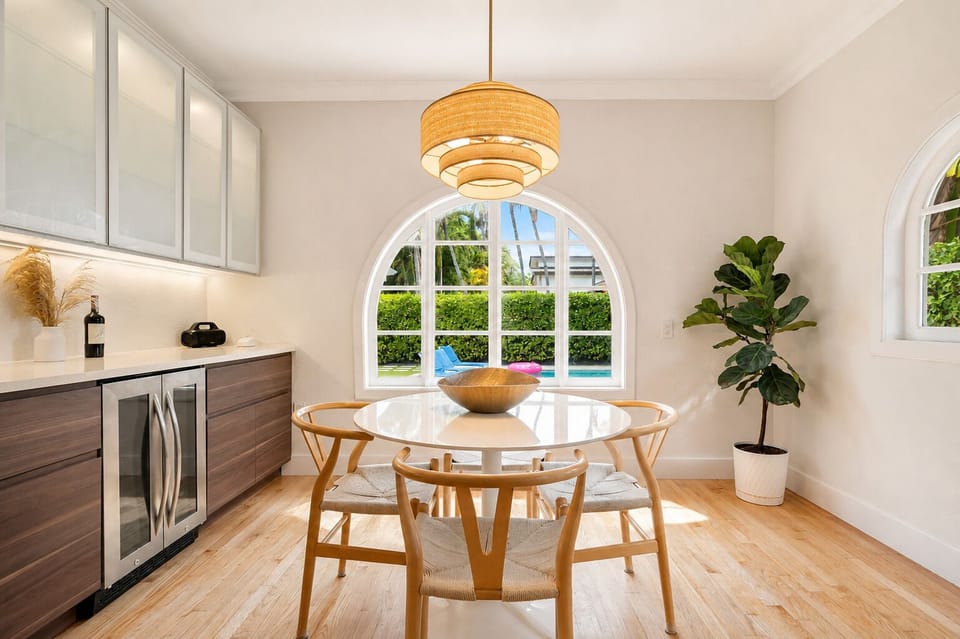 Grab a seat at the round table for breakfast, with an arched window framing the pool right outside. A wine fridge tucked into the counter and a woven pendant overhead make this corner feel extra polished.