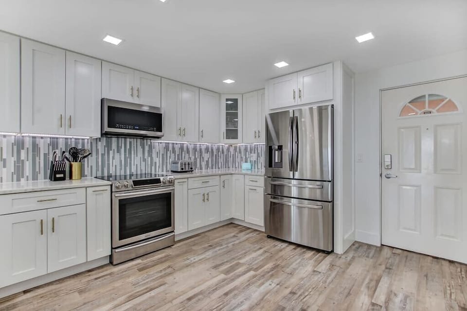 New appliances + Cabinets furnished with pots/pans/utensils/plates/cups.
