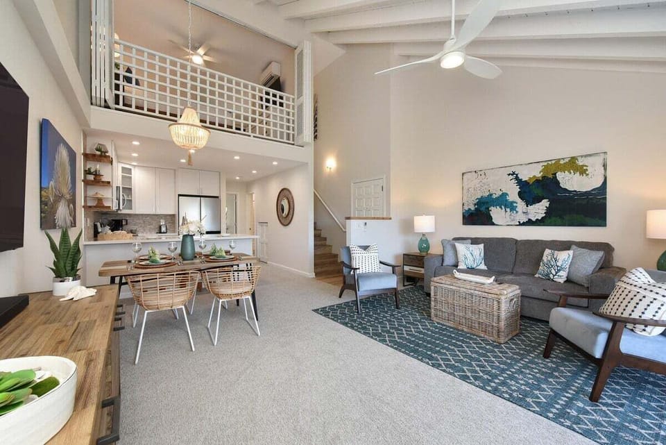 Spacious open‑concept living and dining area with vaulted ceilings, coastal décor, and a bright loft overlooking the great room