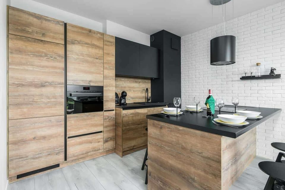 A modern kitchen with wooden cabinets, a grey backsplash, black barstools, and an open design that flows seamlessly into the living space.