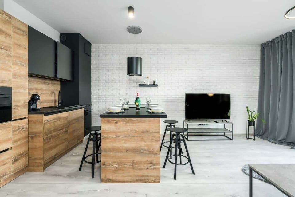  A spacious living room combining modern aesthetics with functionality, featuring a sofa, a flat-screen TV on a wooden stand, and a dining area with a stylish black table and chairs.
