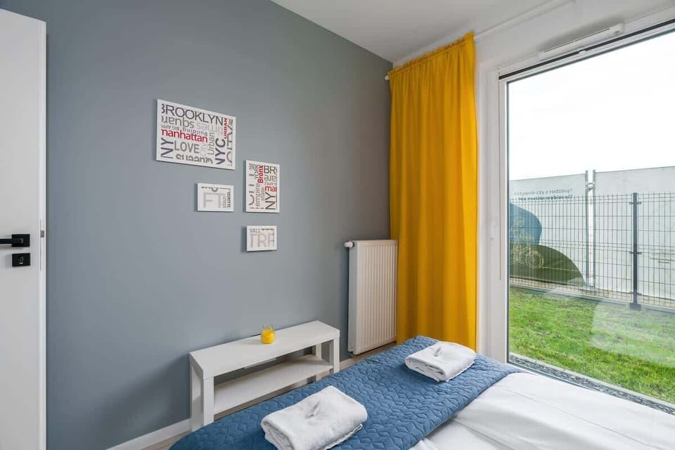 A vibrant bedroom with bright yellow accents in the curtains and decor, a white nightstand, and a large window providing a cheerful ambiance.