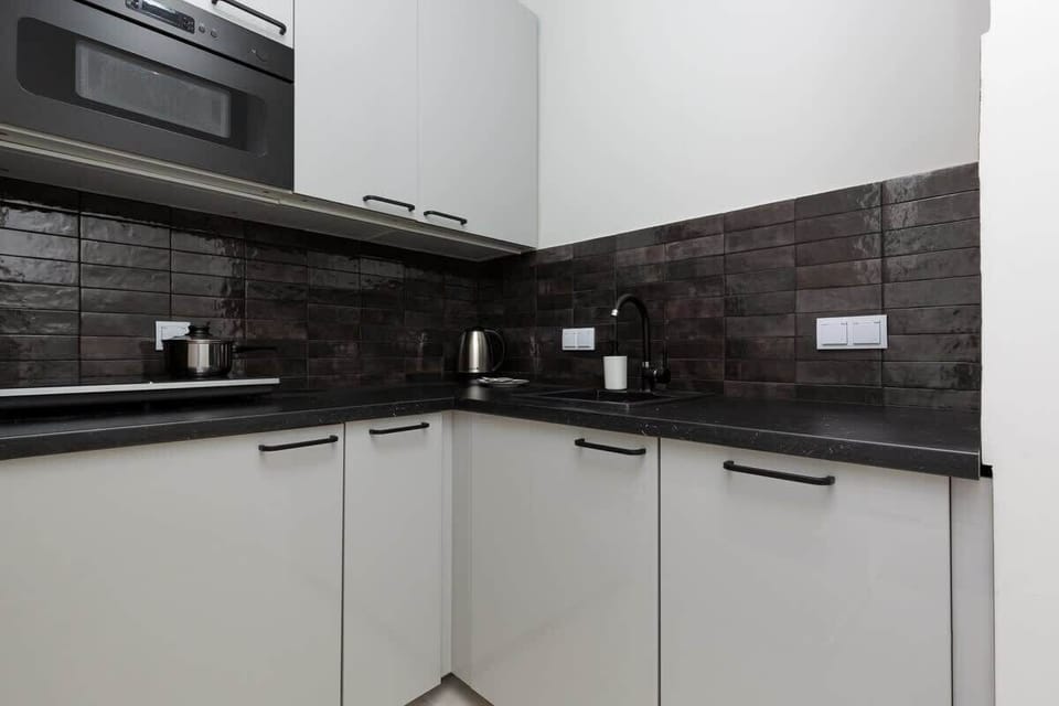 Functional kitchenette with white cabinets and black tiles between the cabinets.