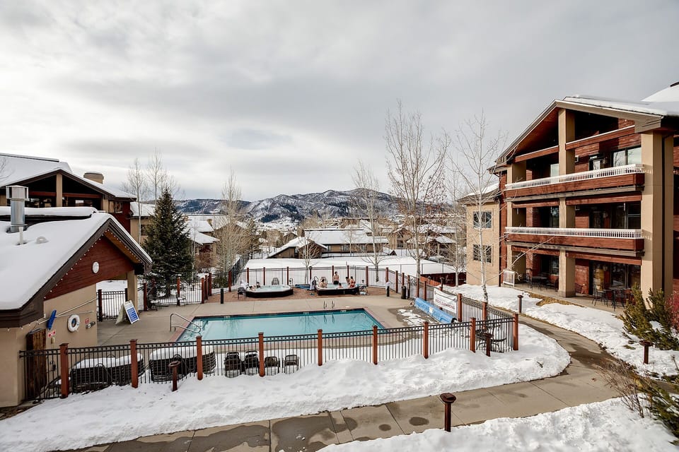 Mountain resort complex featuring outdoor pool and hot tub facilities surrounded by snow-covered peaks and alpine architecture.