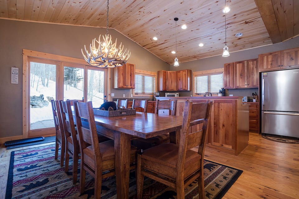 Gather around this stunning wooden dining table where memories are made, with winter views through large windows and a dramatic antler chandelier overhead.