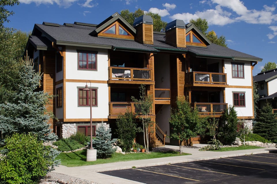 Modern mountain-style building featuring warm wood accents and stone foundation in a beautifully landscaped setting.
