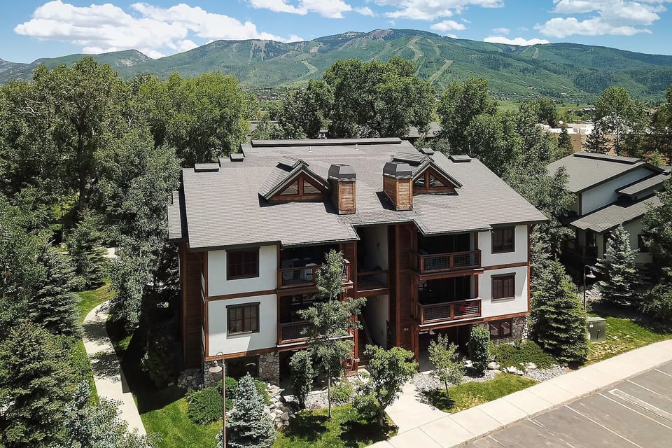 Mountain lodge-style vacation rental nestled among mature trees with stunning alpine views and manicured landscaping.