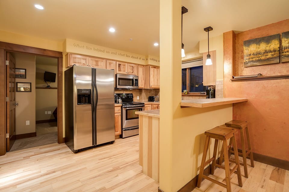 Your fully equipped kitchen features stainless steel appliances, warm wood cabinetry, and a convenient breakfast bar for morning coffee or quick meals.