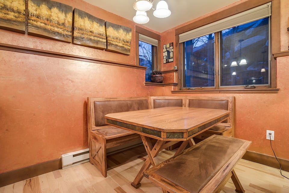 Gather around this cozy corner banquette where warm wood tones and soft lighting create the perfect spot for your morning coffee or evening meals together.