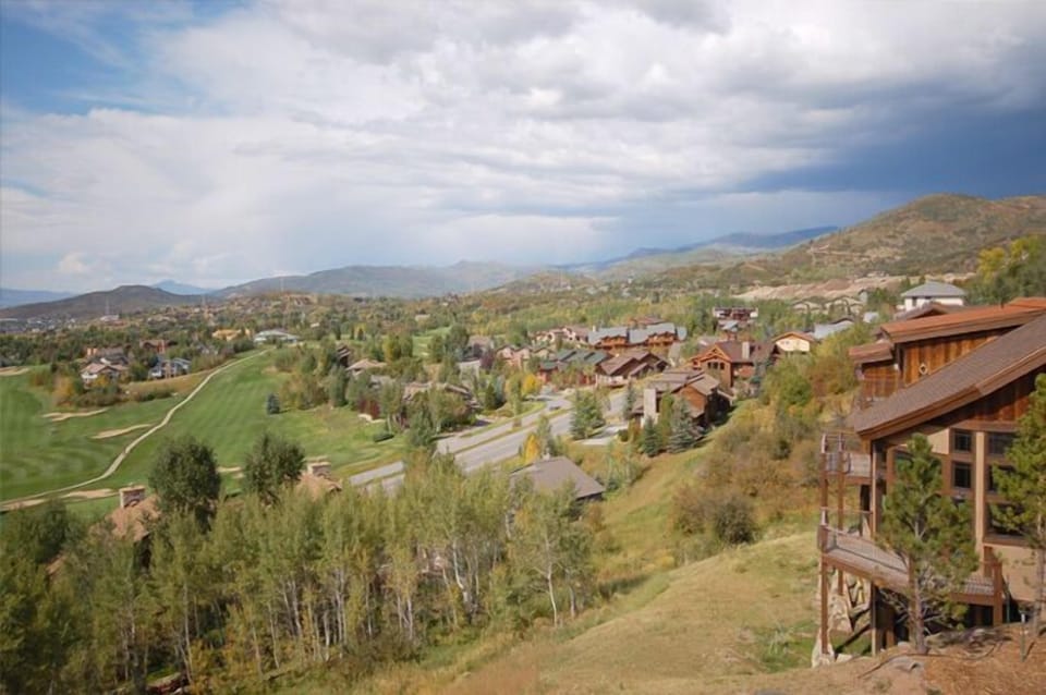 An elevated vantage point reveals the property nestled within a scenic mountain valley, surrounded by residential neighborhoods, rolling terrain, and distant peaks under a partly cloudy sky.
