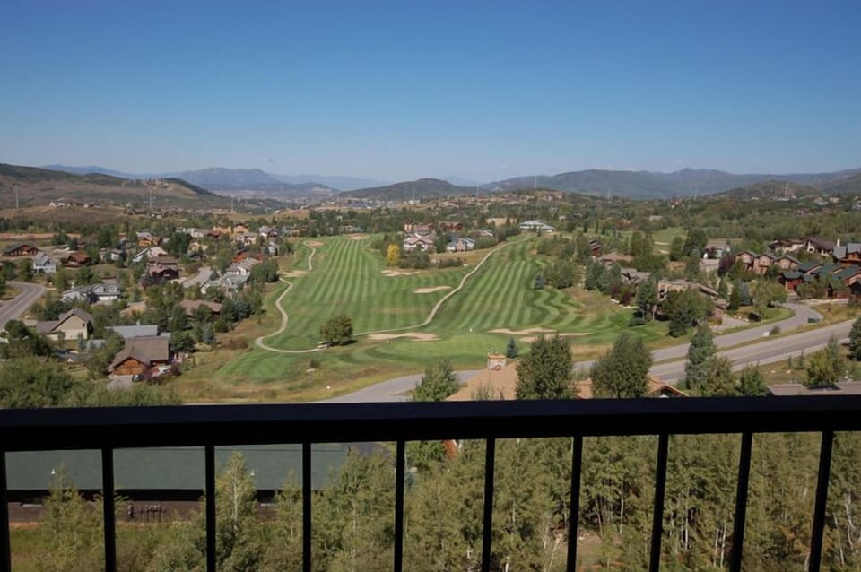 Scenic mountain valley property with rolling golf course views framed by distant peaks and residential hillsides under clear blue skies.