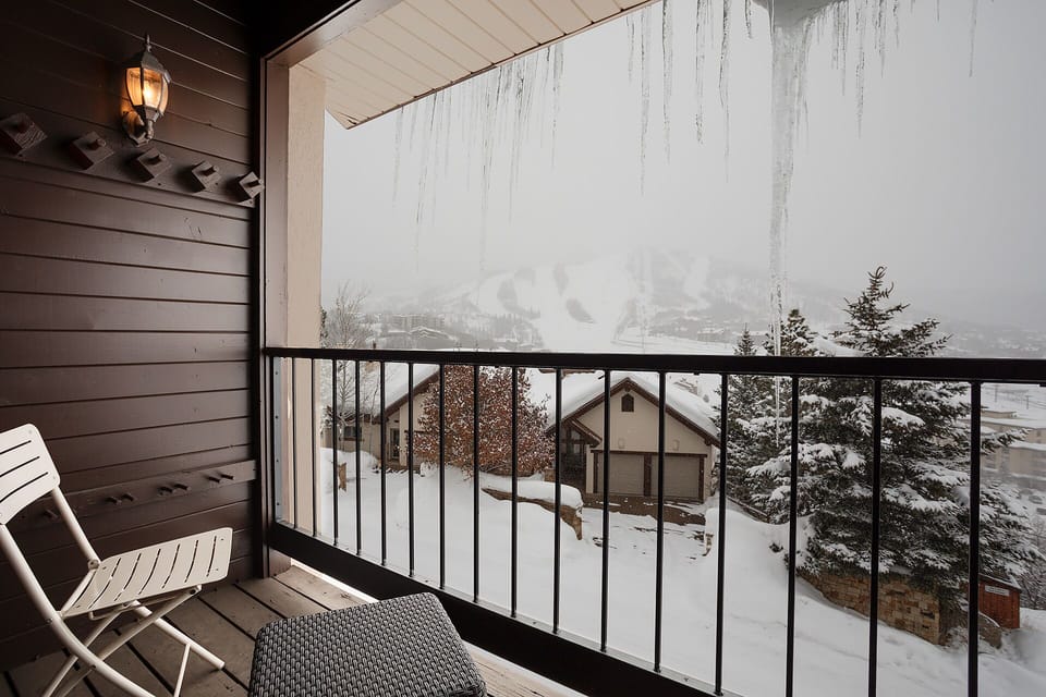 A sheltered balcony overlooking a serene winter landscape with snow-blanketed rooftops and evergreens creating a peaceful mountain escape.