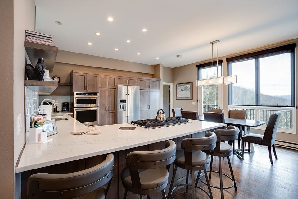 Cook memorable meals in your sleek kitchen featuring premium appliances, spacious island seating, and stunning mountain views through floor-to-ceiling windows.