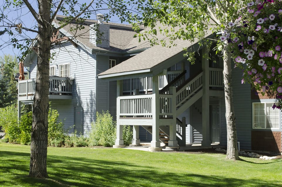 Multi-level vacation property surrounded by mature trees and manicured lawn with flowering garden accents.