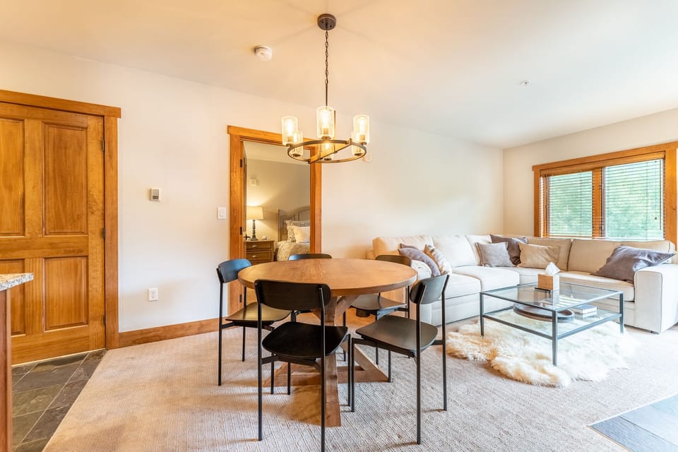 Relax in your bright open-concept living space featuring a cozy sectional sofa, elegant dining table, and warm wood accents throughout.