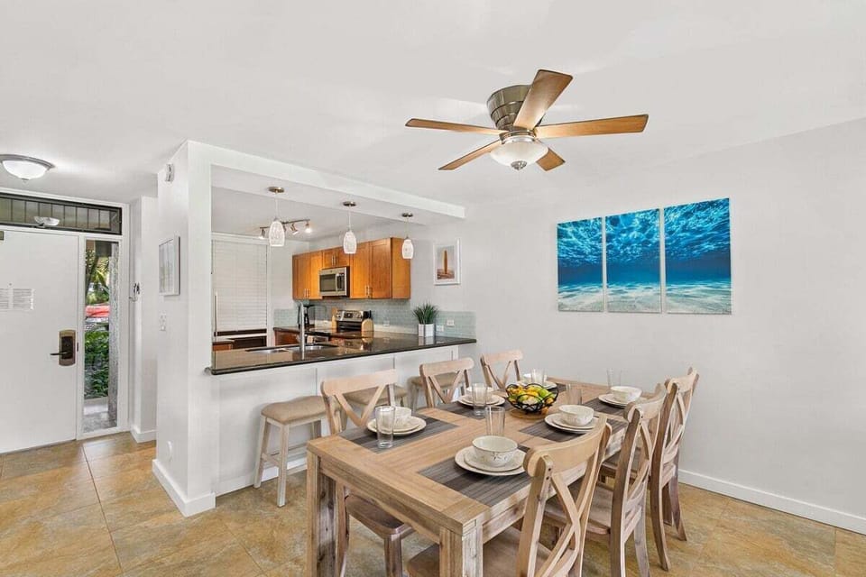 Open dining area with ocean-themed art, ceiling fan, and pass-through kitchen—perfect for casual meals