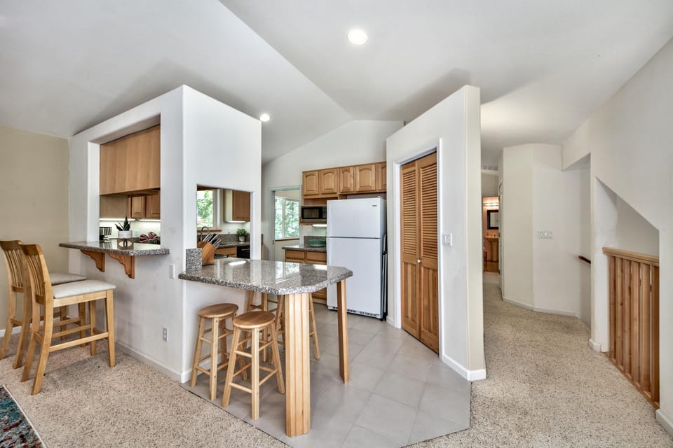Kitchen with granite counters, light wood cabinets, white appliances, and breakfast bar seating on tiled floor.