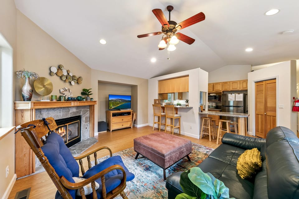 Living room with stone fireplace, blue cushioned rocking chair, leather sofa, and granite breakfast bar with stools.