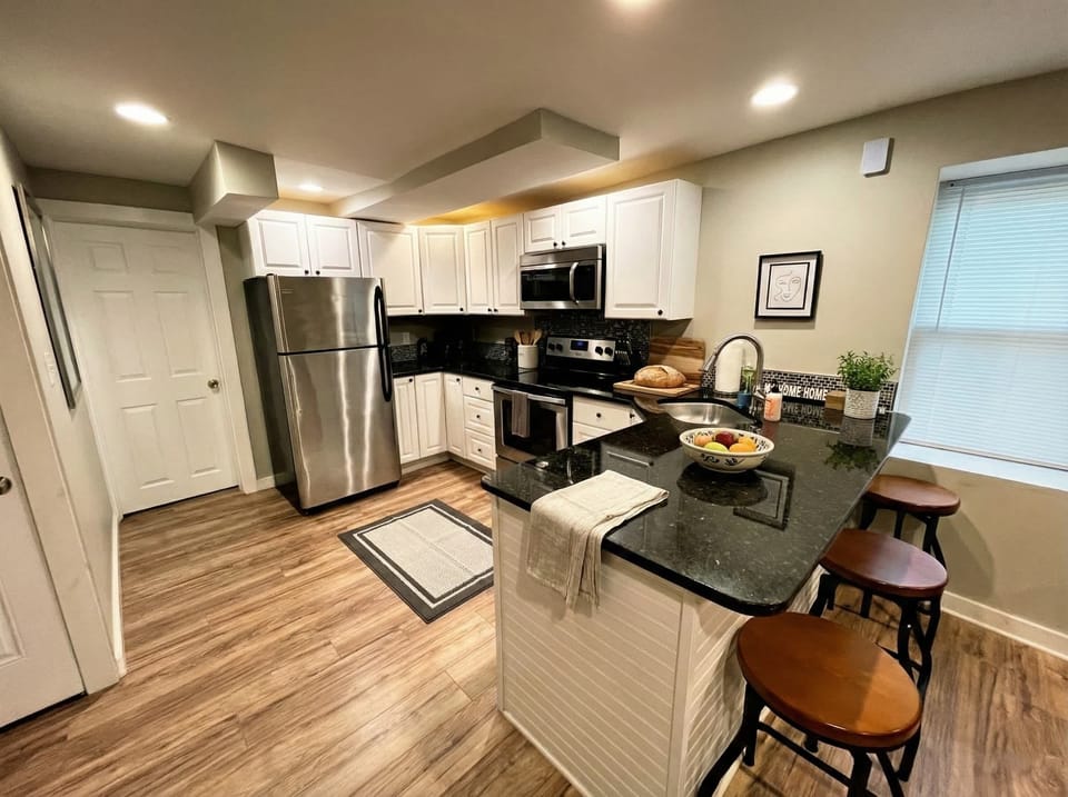 Kitchen with stainless steel appliances, white cabinetry, island seating, and dark counters.