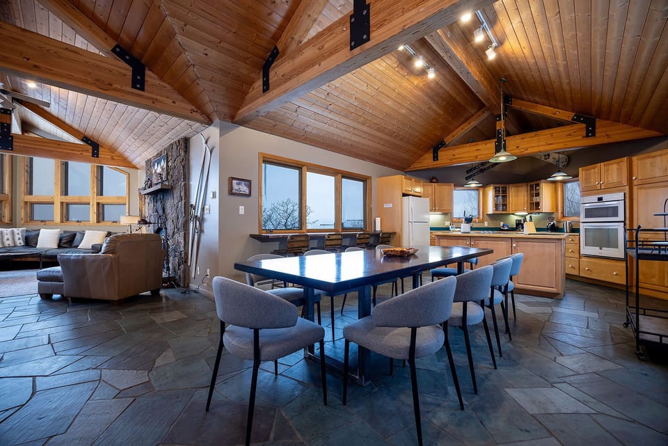 Gather around your spacious dining table beneath soaring wood beams, where the open kitchen invites culinary adventures and stone fireplace promises cozy evenings together.