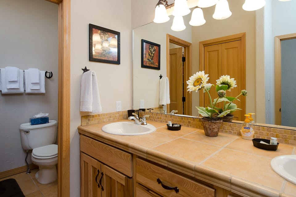 Freshen up in your well-appointed bathroom, featuring a dual-sink vanity with warm tile accents, thoughtful décor, and plenty of towels for your comfort.