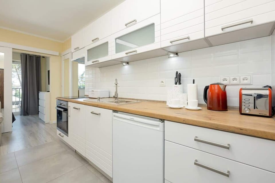 A sleek kitchenette with white cabinetry, a wooden countertop, and modern appliances, arranged in a practical layout.