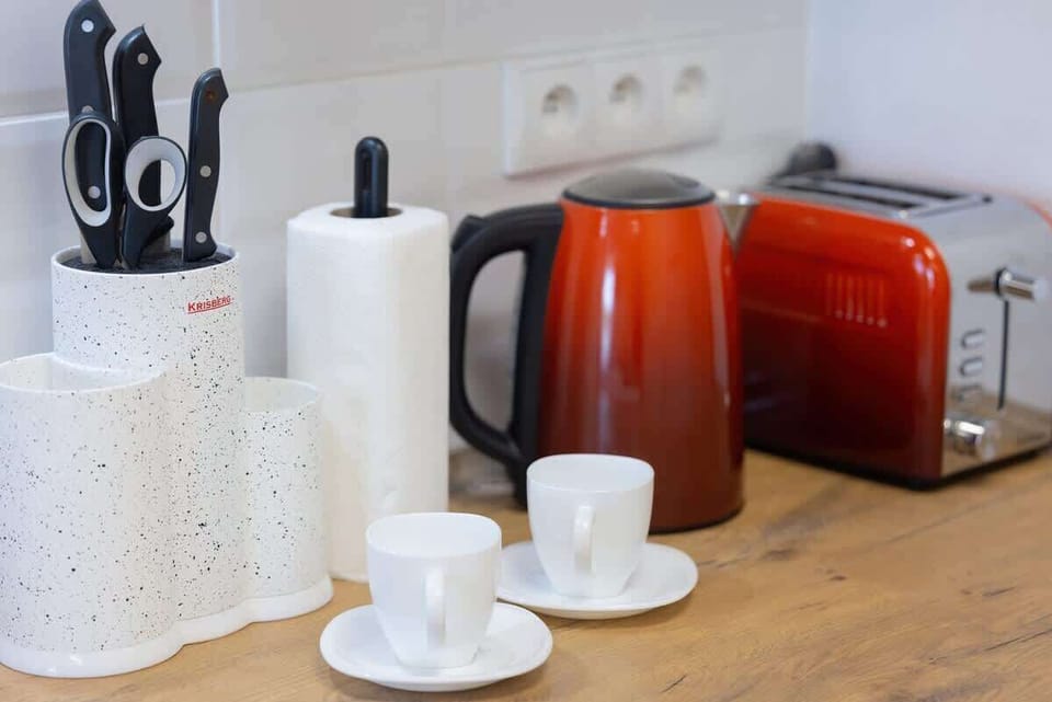 Another view of the kitchen featuring a kettle, red appliances, and neatly arranged crockery for a welcoming feel.