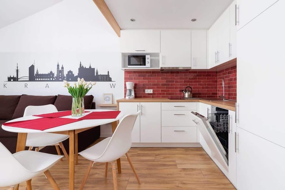 Fully equipped kitchen with modern appliances, red backsplash tiles, and a dining table for two.