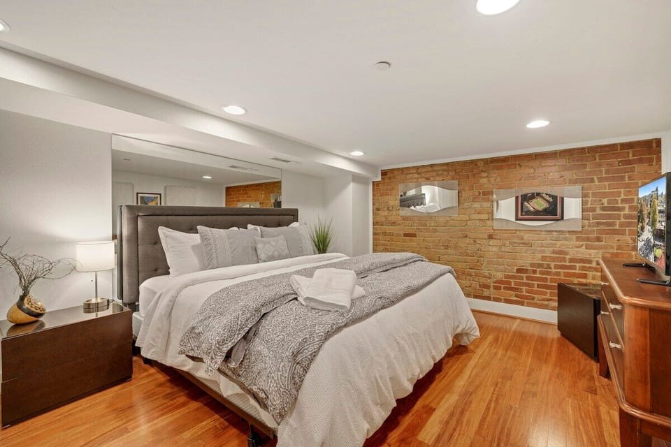 One bedroom features a perfect historic brick wall, a plush King-size bed, a 55-inch Smart TV, and an en suite bathroom