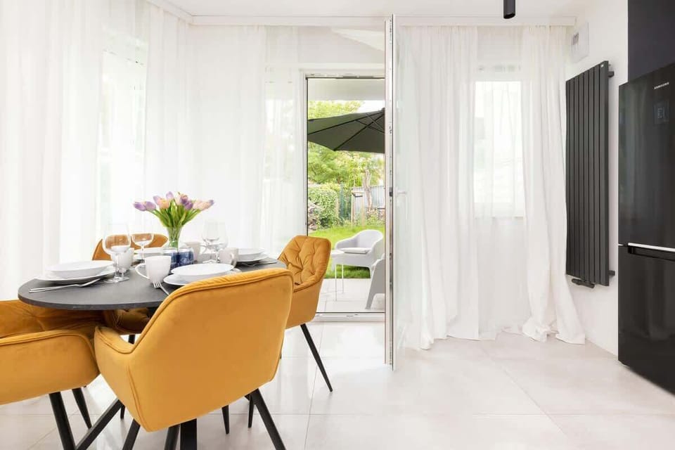 Bright living-dining area with large windows and yellow chairs.