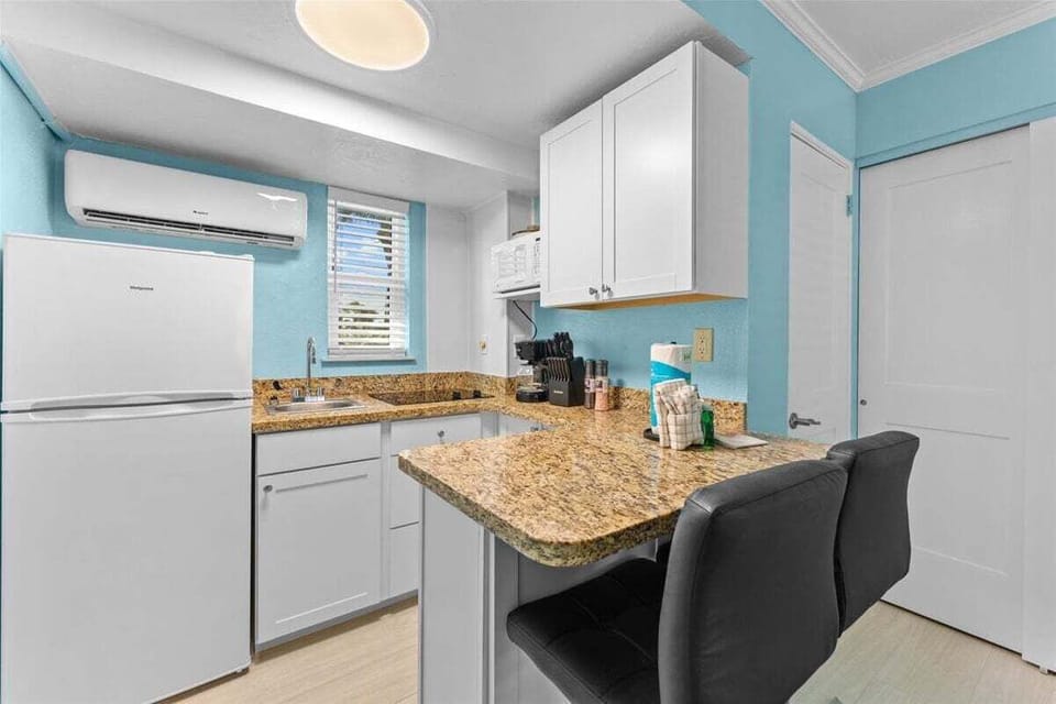 Fully equipped kitchenette with granite counters, white appliances, microwave, and bar seating for two — everything you need for a home-cooked meal.