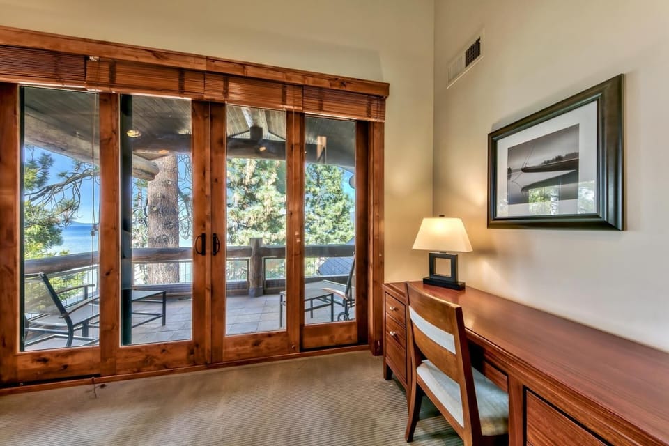 Your private workspace features rich wood furnishings and French doors opening to a balcony with stunning lake views through towering pines.