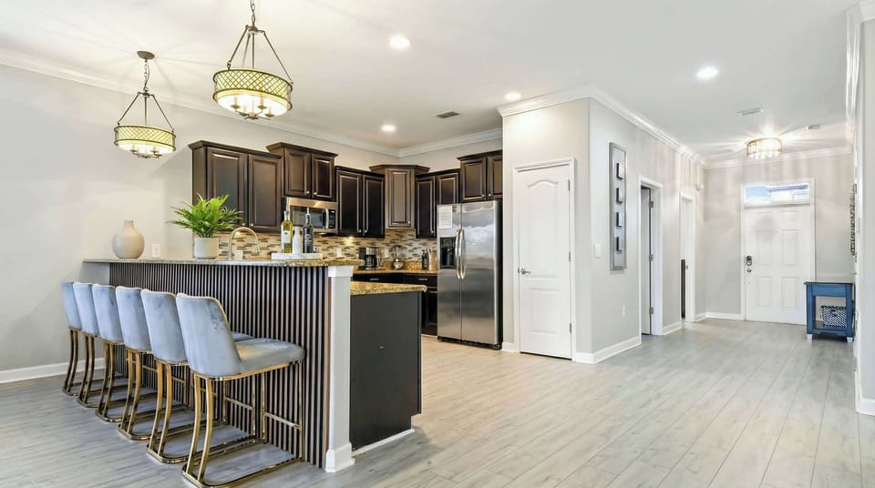Modern kitchen with a breakfast bar, elegant pendant lighting, dark wood cabinets, and stainless steel appliances.
