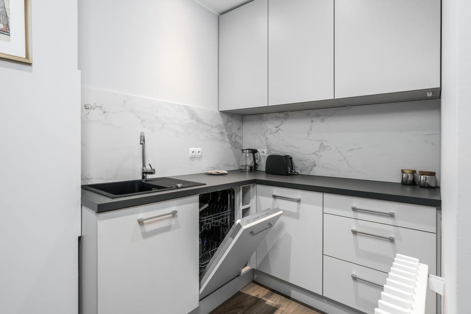  A modern kitchen with white cabinets, a gray countertop, and a tiled backsplash.