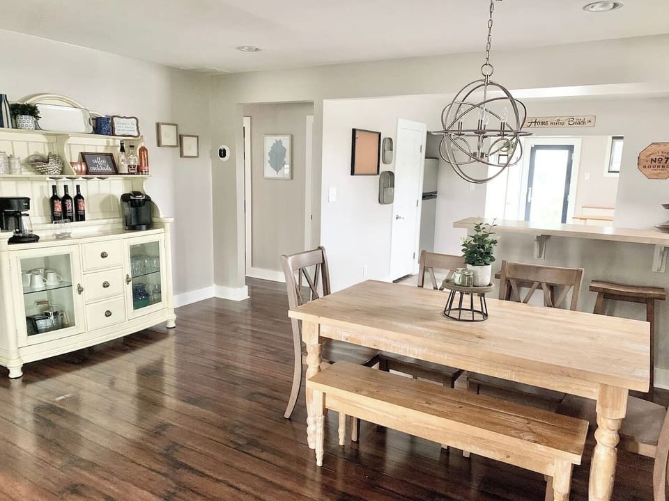 This charming dining area features a farmhouse table with bench seating and a unique orbital chandelier. A white hutch serves as a coffee and wine station, making it easy to enjoy a beverage before heading to the shore.