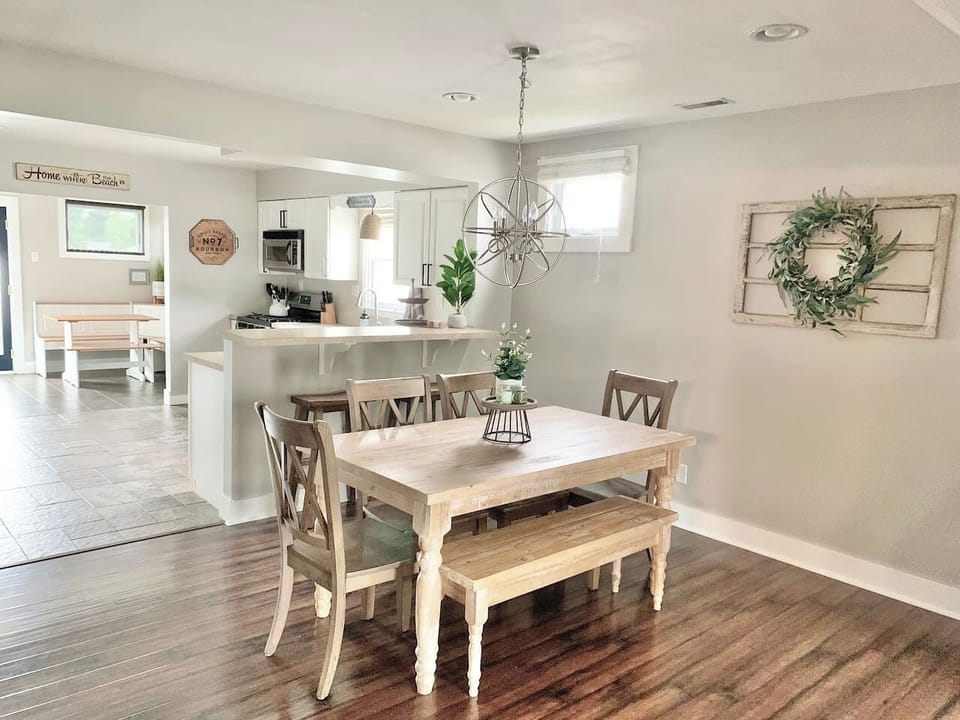 This inviting dining area features a rustic farmhouse table with bench seating and a striking orbital chandelier. The open layout provides a clear view of the kitchen and breakfast nook, making it easy to enjoy meals together during your stay.