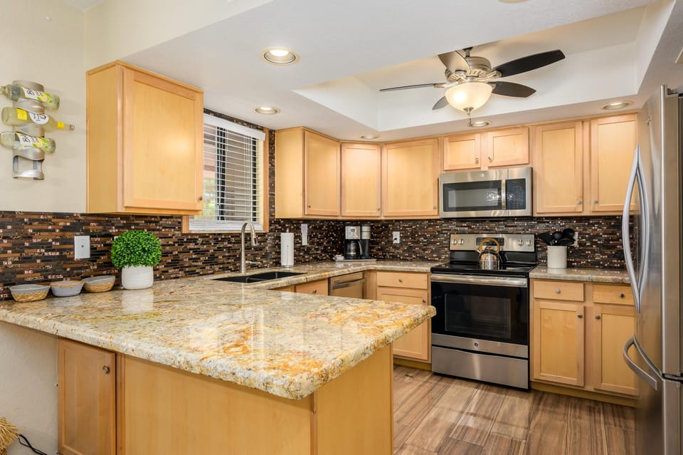 Granite countertop extends into breakfast bar, with light wood cabinets and dark mosaic tile backsplash.