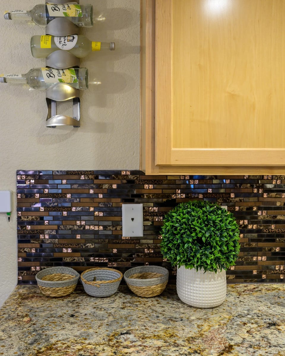 Granite countertop with woven baskets and a white textured planter against a dark mosaic tile backsplash.