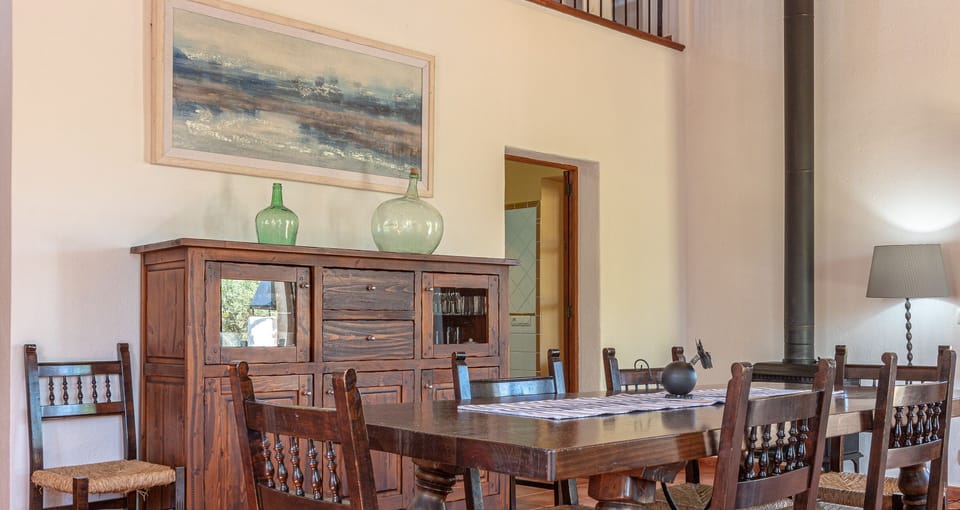 Rustic dining room with wooden table, Mallorcan chairs and wood-burning stove in a traditional finca.