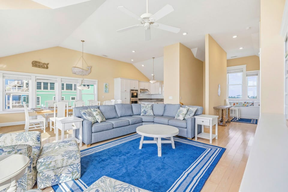 Relax in your spacious open-concept living area with vaulted ceilings, plush sectional seating, and coastal-inspired décor that creates the perfect beach retreat atmosphere.