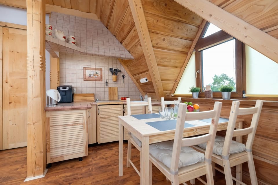 A compact kitchen and dining nook made entirely of light wood, with a rustic dining table and chairs under the sloped ceiling.