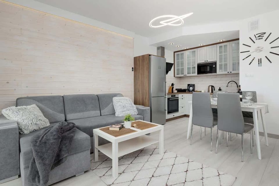 A cozy living room with a light gray corner sofa, a coffee table, and a modern decor theme in soft tones, complemented by a large window for natural light.