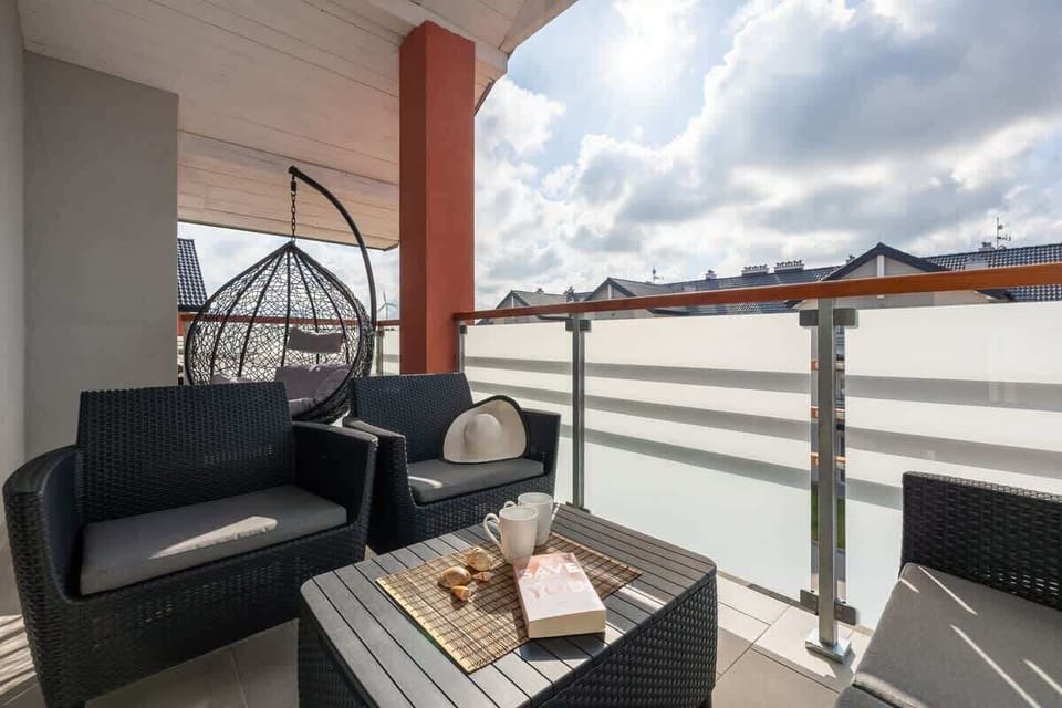 A balcony with a seating area, including black rattan chairs and a small table, offering a view of the surroundings.