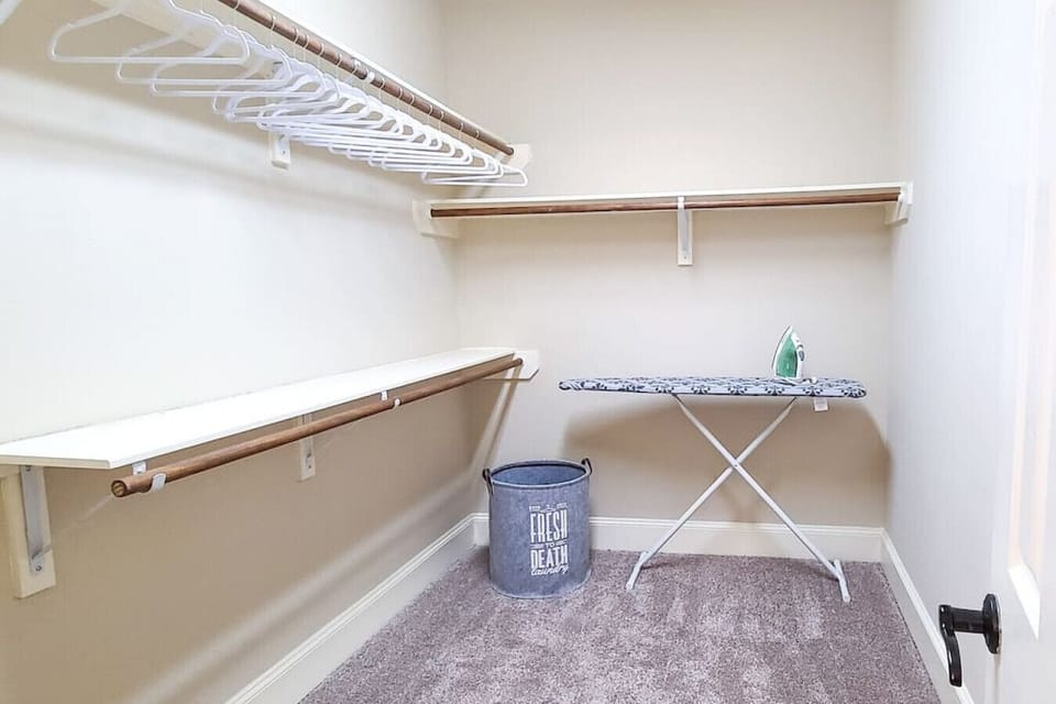 A huge walk-in closet equipped with hangers, an ironing board, an air mattress, and extra sheets and pillows.