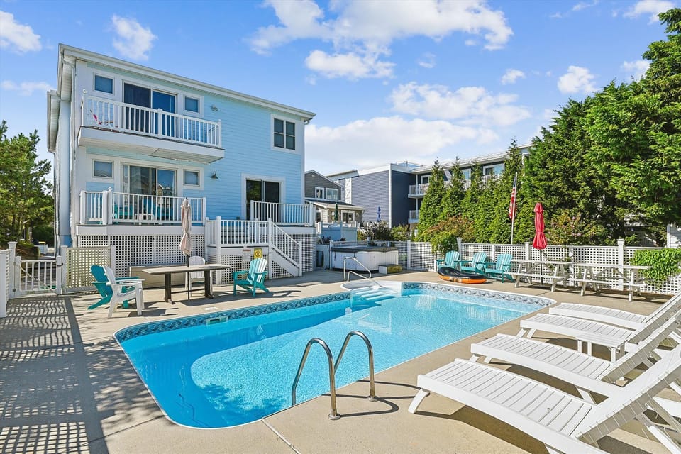 Coastal vacation home featuring a private pool, sunny deck with lounge chairs, and vibrant blue siding. Perfect for relaxing summer getaways near the beach.