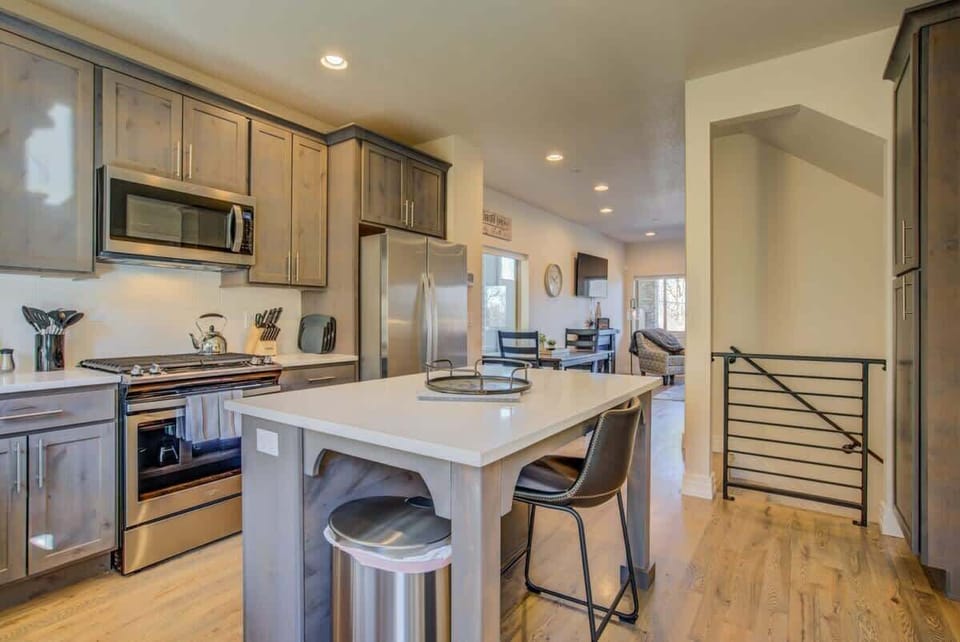 The kitchen centers around a long island with seating, paired with stainless appliances and warm cabinetry. Whether prepping a meal or lingering with coffee, the open layout keeps everything within reach and conversation flowing.
