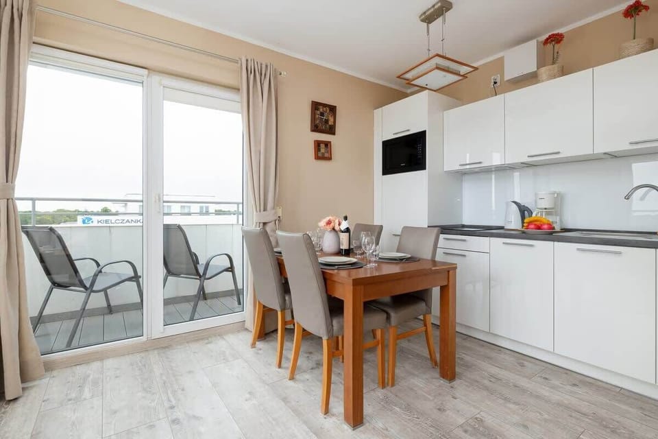 A bright kitchen with a dining area, modern white cabinets, and a small table near a balcony door for convenient access to outdoor space.