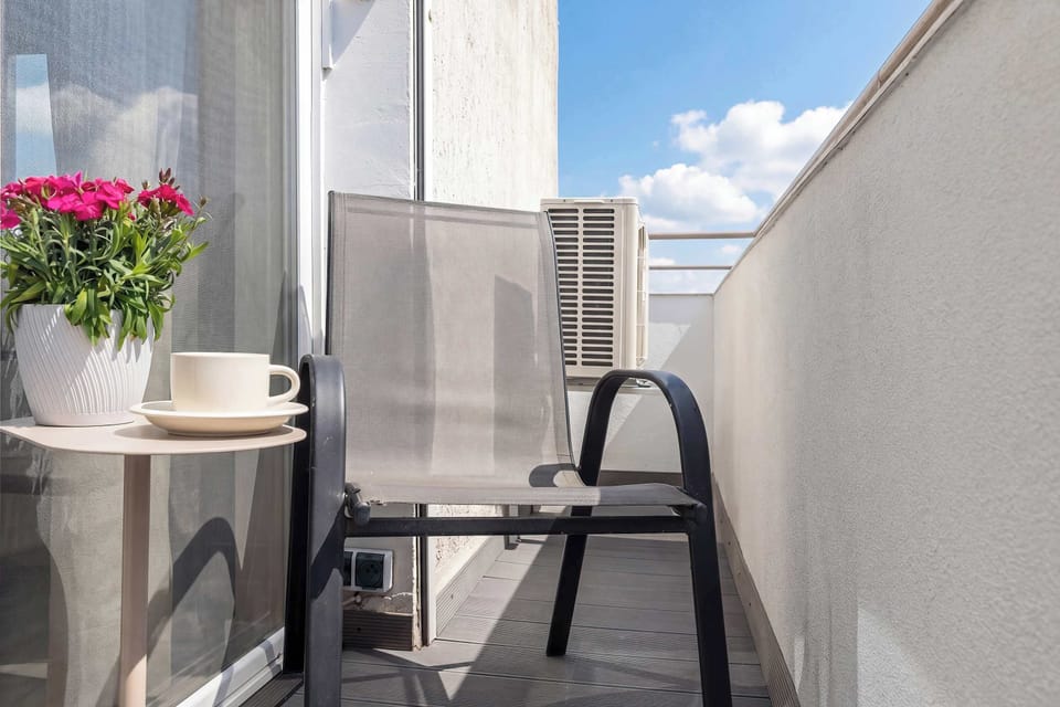 A narrow balcony with a small table and chair, decorated with flowers.