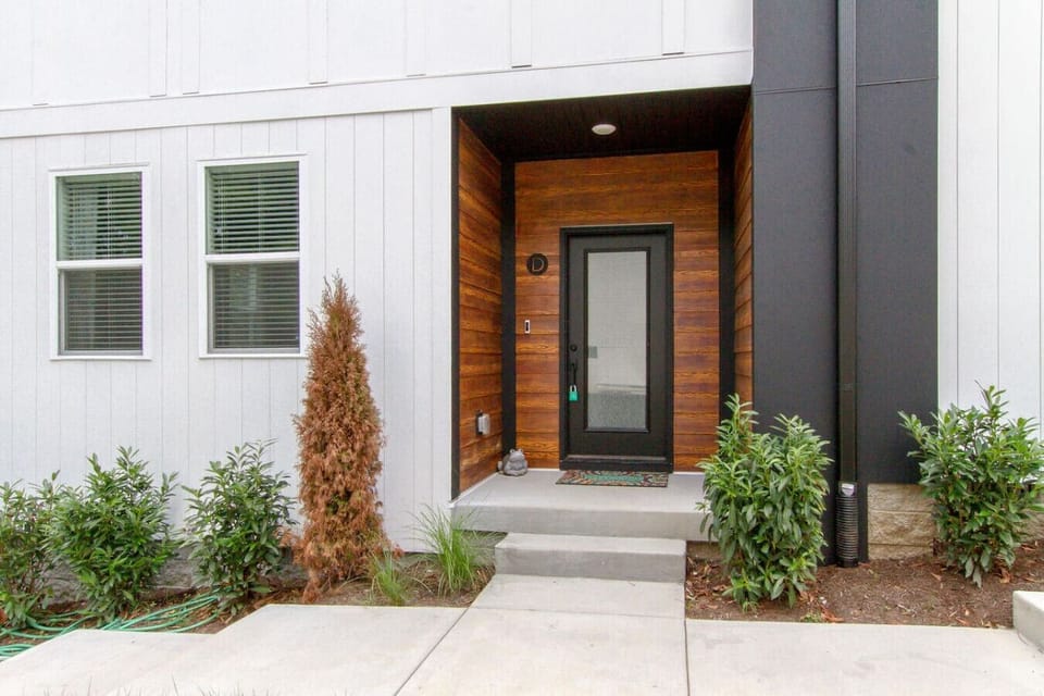 Modern front entrance with dark gray and wood-panel door, steps, and evergreen shrub