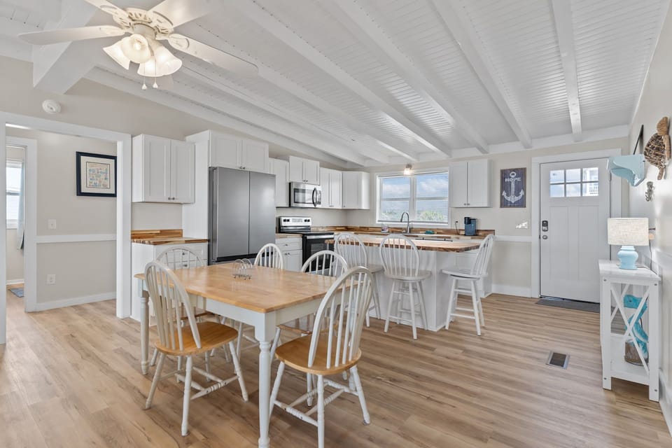 Bright kitchen with white cabinetry, stainless appliances, butcher block counters, and island seating for four, plus coffee maker and window views in this Oak Island, NC beach home.